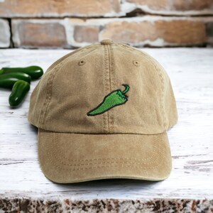 May include: A brown baseball cap with a green embroidered chilli pepper on the front.