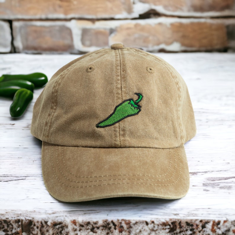 May include: A brown baseball cap with a green embroidered chilli pepper on the front.