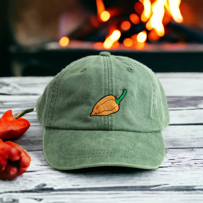 May include: A green baseball cap with an embroidered orange pepper on the front. The cap has a curved brim and a mesh back.