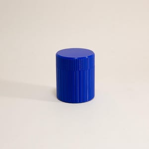 May include: A small, cylindrical container in a vibrant royal blue color. The exterior features a distinct vertical ribbed texture that runs along the sides, and it is topped with a matching flat, circular lid that fits securely on the top.