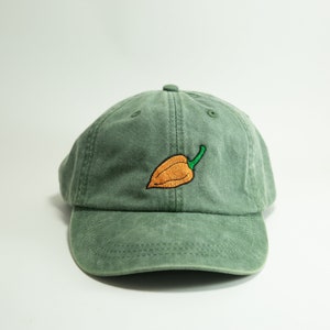 May include: A green cotton baseball cap with an embroidered orange and green pepper on the front.