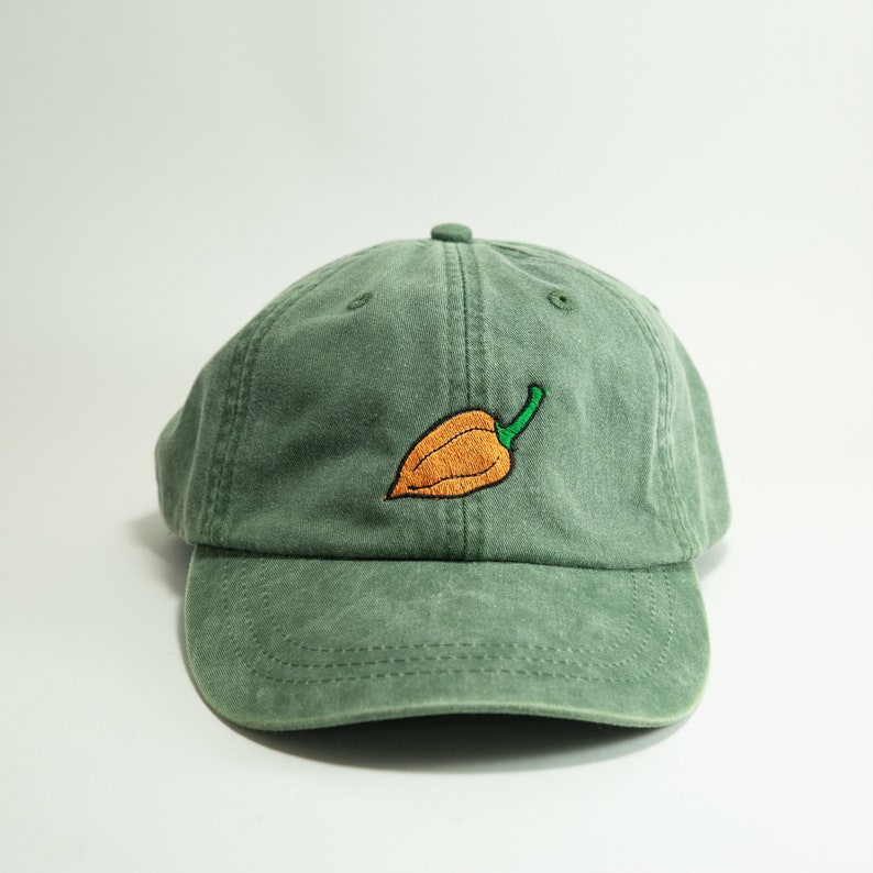 May include: A green cotton baseball cap with an embroidered orange and green pepper on the front.