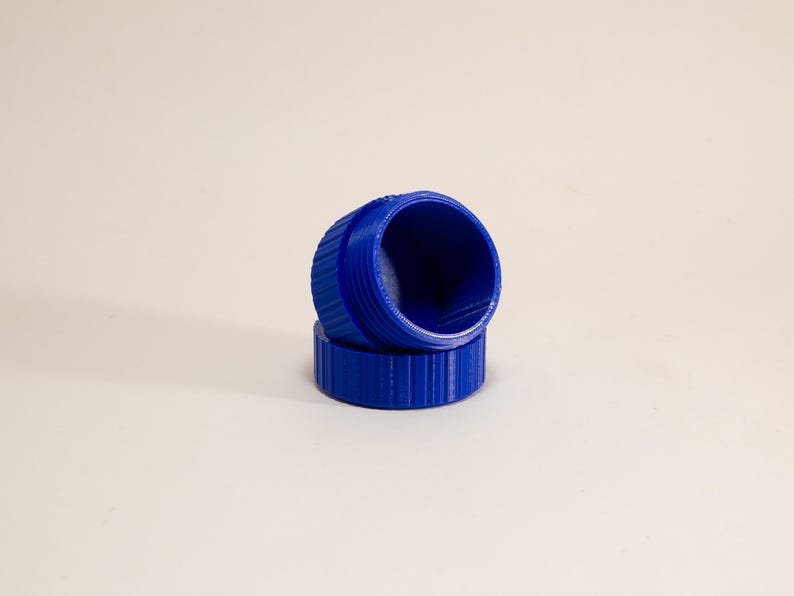 May include: A pair of bright blue plastic caps with a cylindrical shape and a ribbed exterior texture. One cap is positioned upright, while the other rests horizontally beneath it, showcasing the hollow interior and threaded design.