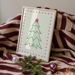 Puede incluir: Una l&aacute;mina enmarcada que muestra un &aacute;rbol de Navidad verde estilizado con una estrella rosa en la punta y adornos coloridos, rodeado por un borde de peque&ntilde;as estrellas rosas sobre un fondo claro, en un marco de madera de color claro.