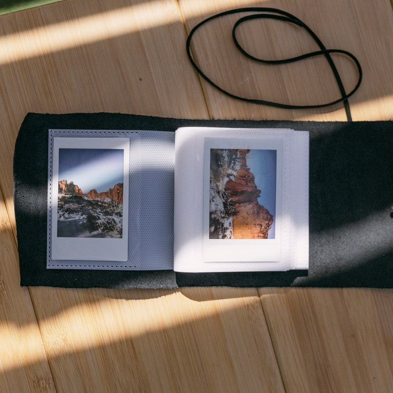 K&ouml;nnte beinhalten: Ein schwarzes Lederfotoalbum mit zwei wei&szlig;en Fotoeins&auml;tzen. Die Fotos zeigen eine Landschaft mit roten Felsformationen.