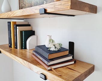 May include: Two wooden shelves with black metal brackets, holding books, vases, and decorative items. The shelves are mounted on a white wall.