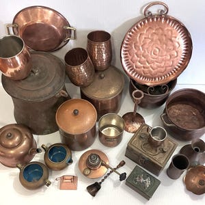 May include: A collection of antique copper kitchenware, including pots, pans, mugs, a teapot, and decorative items. The items vary in size and shape, showcasing a range of textures and designs, with a warm, reddish-brown hue.