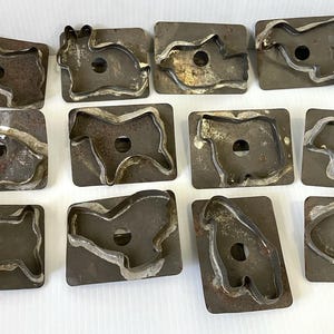 Könnte beinhalten: Eine Sammlung von Vintage-Keksformen aus Metall in verschiedenen Tierformen, darunter ein Hund, ein Kaninchen und ein Fisch. Die Ausstecher haben eine rechteckige Basis mit einem Ausschnittdesign und ein rustikales, gealtertes Aussehen. Die Sammlung wird auf einer weißen Oberfläche präsentiert.