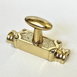 May include: A polished brass door bolt with an oval handle. The rectangular body features decorative detailing and mounting holes. The bolt is a bright gold color and is designed for securing doors or cabinets.