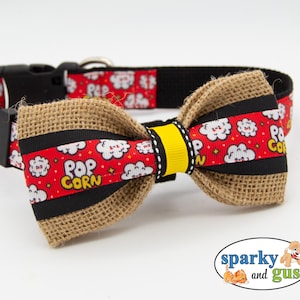 May include: A dog collar with a popcorn-themed bow tie. The collar is black with a red popcorn pattern. The bow tie is burlap with black and yellow accents and a red popcorn pattern. The collar has a black plastic buckle.