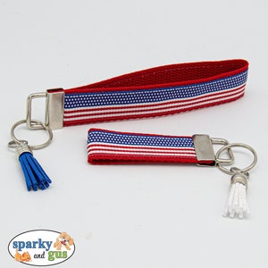 May include: Two keychains with red, white, and blue striped fabric and silver key rings. One keychain has a blue tassel and the other has a white tassel.