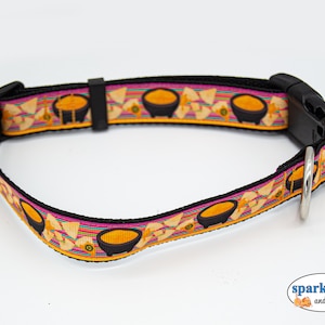 May include: A black dog collar with a colorful pattern of yellow, orange, pink, and black. The pattern features a repeated image of a bowl of nacho cheese and tortilla chips. The collar has a black plastic buckle and a silver metal D-ring.