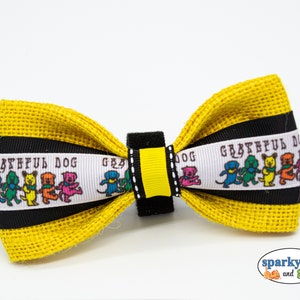 May include: A yellow burlap bow tie with a black and white ribbon featuring a line of dancing dogs and the text "Grateful Dog".
