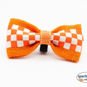 May include: Orange and white checkered bow tie with burlap accents. The bow tie is attached to a black elastic band.