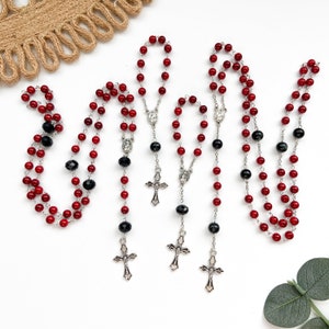 May include: Three red and black rosary beads with silver crucifixes and centerpieces. The beads are strung on a silver chain.
