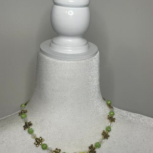 May include: A green and gold beaded necklace with bee charms and a yellow flower charm.