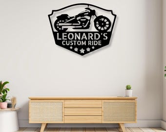 May include: A black metal wall sign shaped like a shield featuring a silhouette of a motorcycle at the top. The text "LEONARD'S CUSTOM RIDE" is cut out in the center, and four small star shapes are positioned along the bottom edge of the sign.