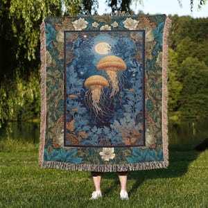 May include: A woven tapestry blanket featuring a nighttime ocean scene with two jellyfish, a full moon, and aquatic plants. The blanket has a blue, green, and tan color scheme with a fringed edge. The blanket is approximately 60 inches wide and 80 inches long.