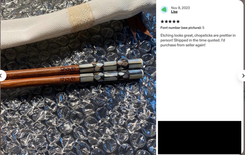 K&ouml;nnte beinhalten: Ein Paar Essst&auml;bchen aus Holz mit dem eingravierten Namen Shayla im braunen Holz und einem dekorativen Griffbereich, der mit einem geometrischen Muster aus schillernden wei&szlig;en und dunkelgrauen Muschelst&uuml;cken eingelegt ist, auf Luftpolsterfolie.
