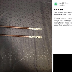 K&ouml;nnte beinhalten: Ein Paar braune Essst&auml;bchen aus Holz mit einem dekorativen silberfarbenen Metallband am Griffende, das ein geometrisches Ausschnittmuster aufweist. Die St&auml;bchen haben ein glattes, konisches Design und liegen horizontal vor einem dunklen Hintergrund.