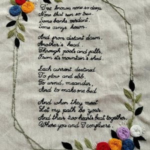 Könnte beinhalten: Ein besticktes Gedicht auf einem weißen Stoffhintergrund mit einem floralen Design in den Ecken. Das Gedicht lautet: "Ich habe keinen so tiefen gekannt Keinen, der so wahr fließt. Manche Ufer sind grün, Manche Schluchten sind gehauen. Und aus der fernen Morgendämmerung, Ein anderer Kopf. Durch Becken und Fälle. Aus seinem Berg abgeschieden. Jeder Strom ist dazu bestimmt Zu fließen und zu ebben. Sich zu winden, zu mäandern. Und ein Bett zu machen Und wenn sie sich treffen Lass meinen Weg dein sein. Und ihre beiden Herzen schlagen zusammen, Wo du und ich zusammenfließen."