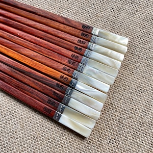 May include: A set of ten wooden chopsticks with a reddish-brown finish, each featuring the black Chinese characters 徐府 printed on the handle. The ends are capped with a white, pearlescent material separated by a silver-toned metal band.