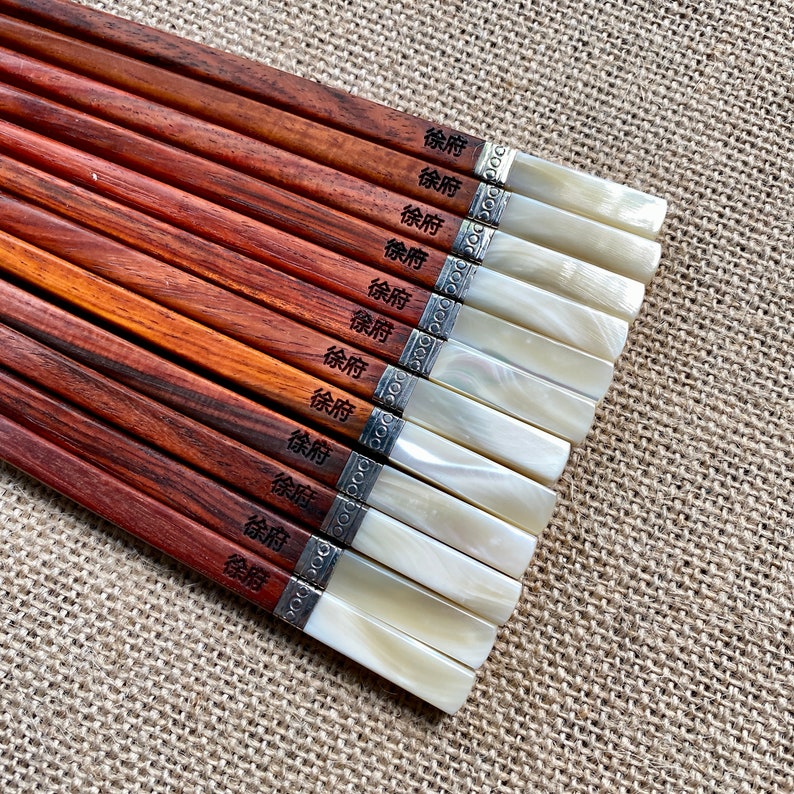 May include: A set of ten wooden chopsticks with a reddish-brown finish, each featuring the black Chinese characters 徐府 printed on the handle. The ends are capped with a white, pearlescent material separated by a silver-toned metal band.