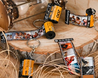 May include: Four yellow and black film canisters with photos printed on the film strips. The canisters are attached to key rings. The canisters are on a wooden surface with brown grass.