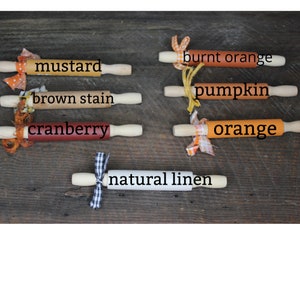 May include: A set of ten rolling pins in various fall colors, including mustard, brown stain, cranberry, burnt orange, pumpkin, orange, and natural linen. The rolling pins are decorated with fabric scraps and ribbons.