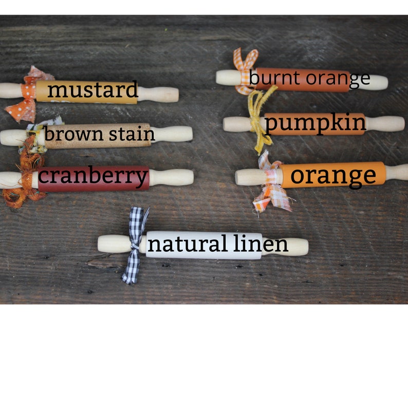 May include: A set of ten rolling pins in various fall colors, including mustard, brown stain, cranberry, burnt orange, pumpkin, orange, and natural linen. The rolling pins are decorated with fabric scraps and ribbons.