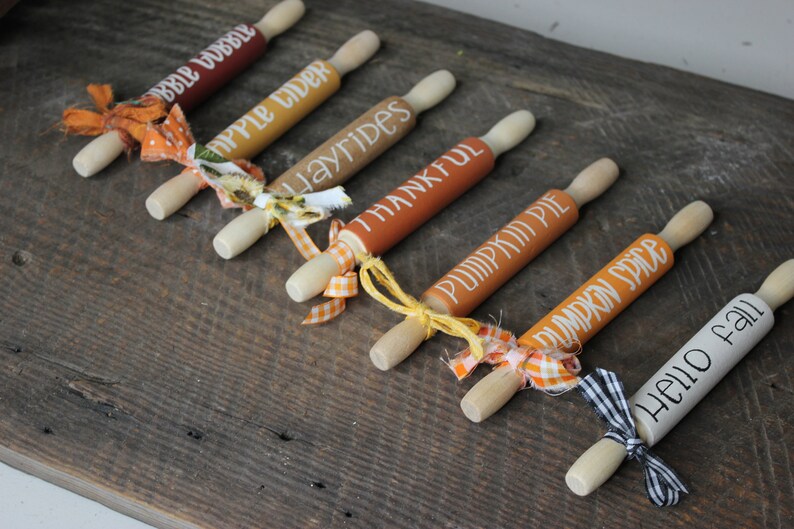 May include: Seven miniature rolling pins with fall-themed sayings, including "Apple Cider", "Hayrides", "Pumpkin Pie", and "Hello Fall". Each pin is decorated with a different colored ribbon.