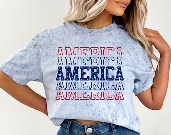 May include: A light blue t-shirt with a distressed look featuring the word "AMERICA" repeated in red, white, and blue with stars.