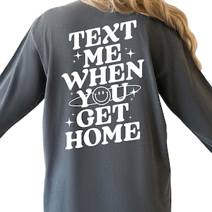 May include: A dark gray long-sleeved shirt with the text "TEXT ME WHEN YOU GET HOME" in white lettering. A smiley face is included in the text.