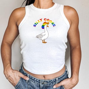 Op de afbeelding: Witte tanktop met een cartoon gans met een regenboog cowboyhoed. De tekst "SILLY GOOSE" staat in regenboogkleuren boven de gans. De tanktop is mouwloos en heeft een racerback ontwerp.