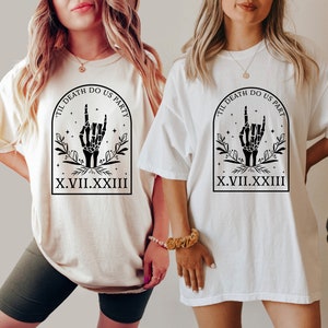 May include: Two white t-shirts with a black graphic design. The graphic features a skeleton hand making a rock and roll hand gesture with the text "Til Death Do Us Part" and "X.VII.XXIII" below.