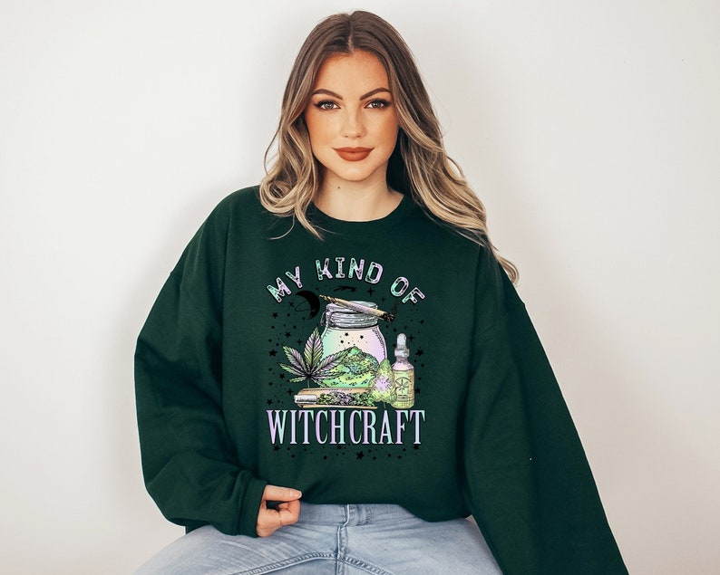 Może przedstawiać: Zielony sweter z nadrukiem "My Kind of Witchcraft" w białym i czarnym kolorze. Wz&oacute;r przedstawia słoik z zieloną rośliną, papier do zwijania i butelkę oleju.