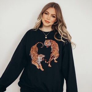 May include: A black sweatshirt with a graphic print of two tigers facing each other. The tigers are orange and black with white stripes.