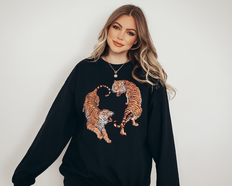 May include: A black sweatshirt with a graphic print of two tigers facing each other. The tigers are orange and black with white stripes.