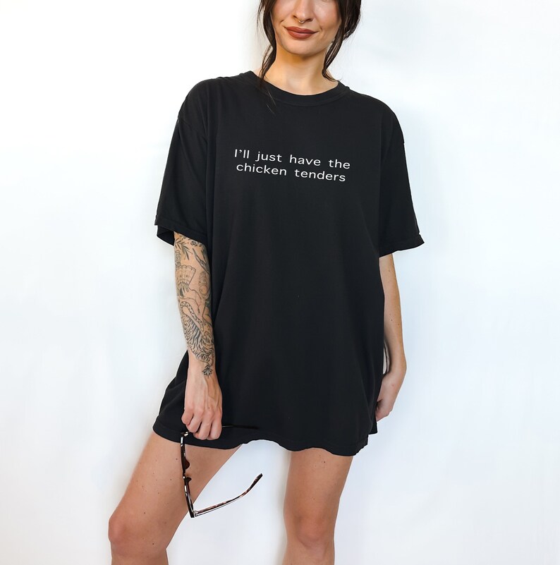 May include: Black oversized t-shirt with the text "I'll just have the chicken tenders" printed in white.