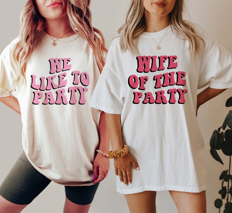 May include: Two white t-shirts with pink text. One shirt says "We Like To Party" and the other says "Wife Of The Party".