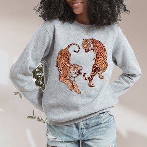 May include: A gray sweatshirt with a graphic print of two orange tigers facing each other. The tigers are in a circular design.