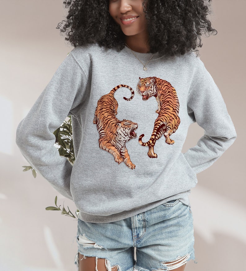 May include: A gray sweatshirt with a graphic print of two orange tigers facing each other. The tigers are in a circular design.