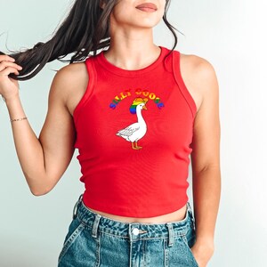 Op de afbeelding: Een rode tanktop met een afbeelding van een witte gans met een regenbooghoed. De tekst "SILLY GOOSE" staat in regenboogkleuren boven de gans. De tanktop is mouwloos en heeft een ronde hals.