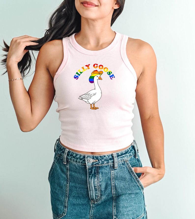 Op de afbeelding: Een lichtroze tanktop met een cartoon gans met een regenboog cowboyhoed. De tekst "SILLY GOOSE" staat boven de gans. De tanktop wordt gecombineerd met een blauwe spijkerbroek.