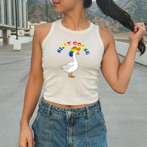 Op de afbeelding: Cr&egrave;mekleurige tanktop met een cartoon gans met een regenboog cowboyhoed. De tekst "SILLY GOOSE" staat in regenboogkleuren boven de gans. De tanktop is mouwloos en heeft een ronde halslijn.