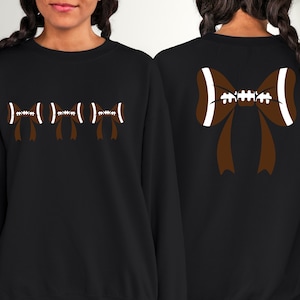 Puede incluir: Sudadera negra con dise&ntilde;o de lazo de f&uacute;tbol americano. La parte delantera muestra tres lazos de f&uacute;tbol, mientras que la trasera presenta un lazo m&aacute;s grande. Los lazos son marrones con detalles blancos, creando un look deportivo y elegante. Para los fan&aacute;ticos del f&uacute;tbol.