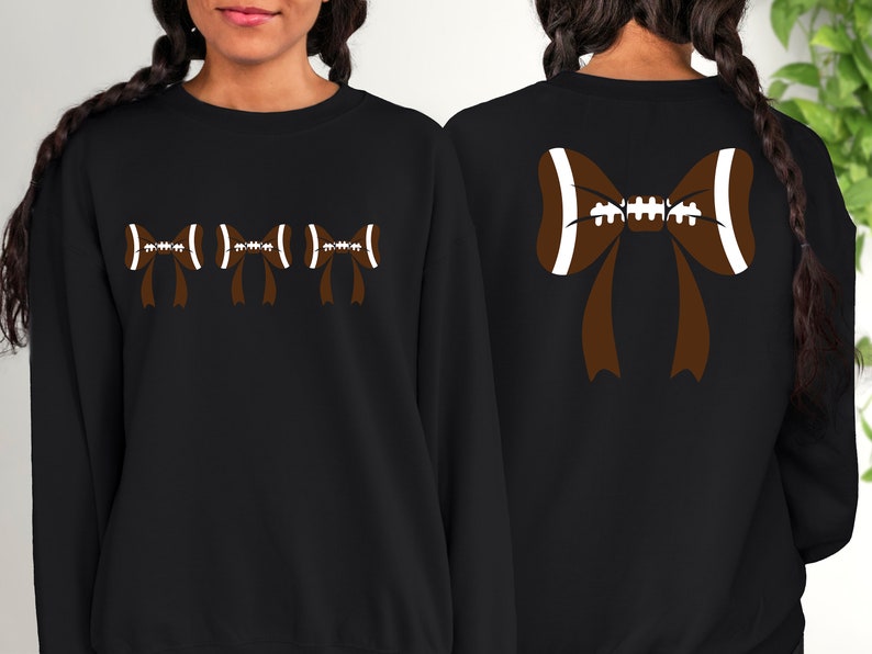 Puede incluir: Sudadera negra con dise&ntilde;o de lazo de f&uacute;tbol americano. La parte delantera muestra tres lazos de f&uacute;tbol, mientras que la trasera presenta un lazo m&aacute;s grande. Los lazos son marrones con detalles blancos, creando un look deportivo y elegante. Para los fan&aacute;ticos del f&uacute;tbol.