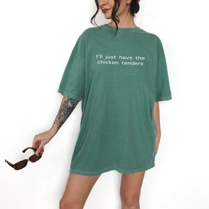 May include: An oversized green t-shirt with the text "I'll just have the chicken tenders" printed in white.