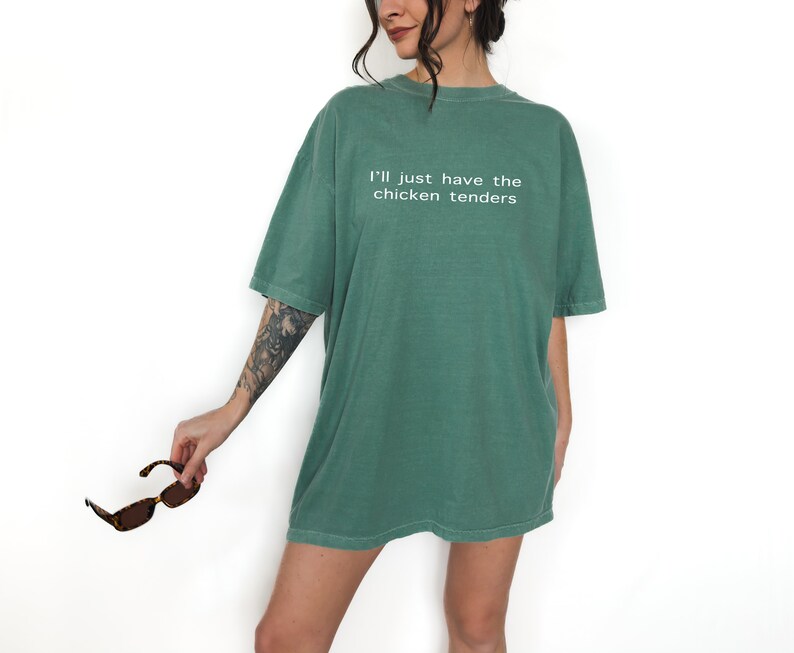 May include: An oversized green t-shirt with the text "I'll just have the chicken tenders" printed in white.