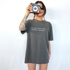 May include: An oversized t-shirt in a dark grey colour with the text "I'll just have the chicken tenders" printed in white on the front.
